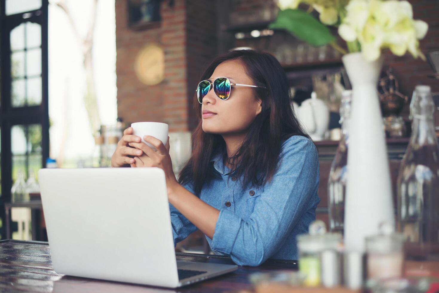 jolie jeune femme hipster assise dans un café avec son ordinateur portable, détourna les yeux et sourit heureux, se détendre avec des vacances, concept de style de vie de femme. photo