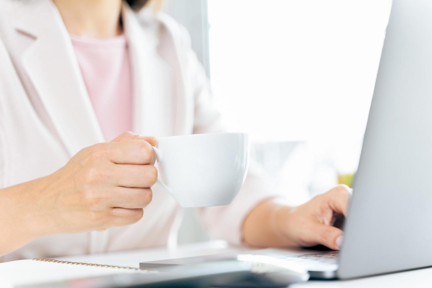 gros plan d'une femme d'affaires utilisant un ordinateur portable et assis au bureau, tenant une tasse de café. photo