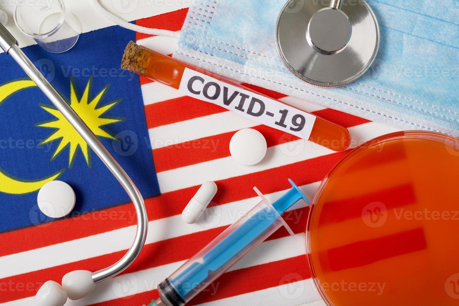 coronavirus, le concept covid-19. vue de dessus masque respiratoire protecteur, stéthoscope, seringue, pilules sur le drapeau de la malaisie. photo