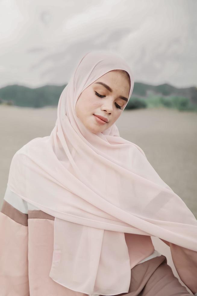 beau modèle féminin islamique portant la mode hijab, une robe de mariée moderne pour femme musulmane assise dans le sable et la plage. portrait d'une fille asiatique modèle utilisant le hijab s'amusant à la plage avec des arbres photo