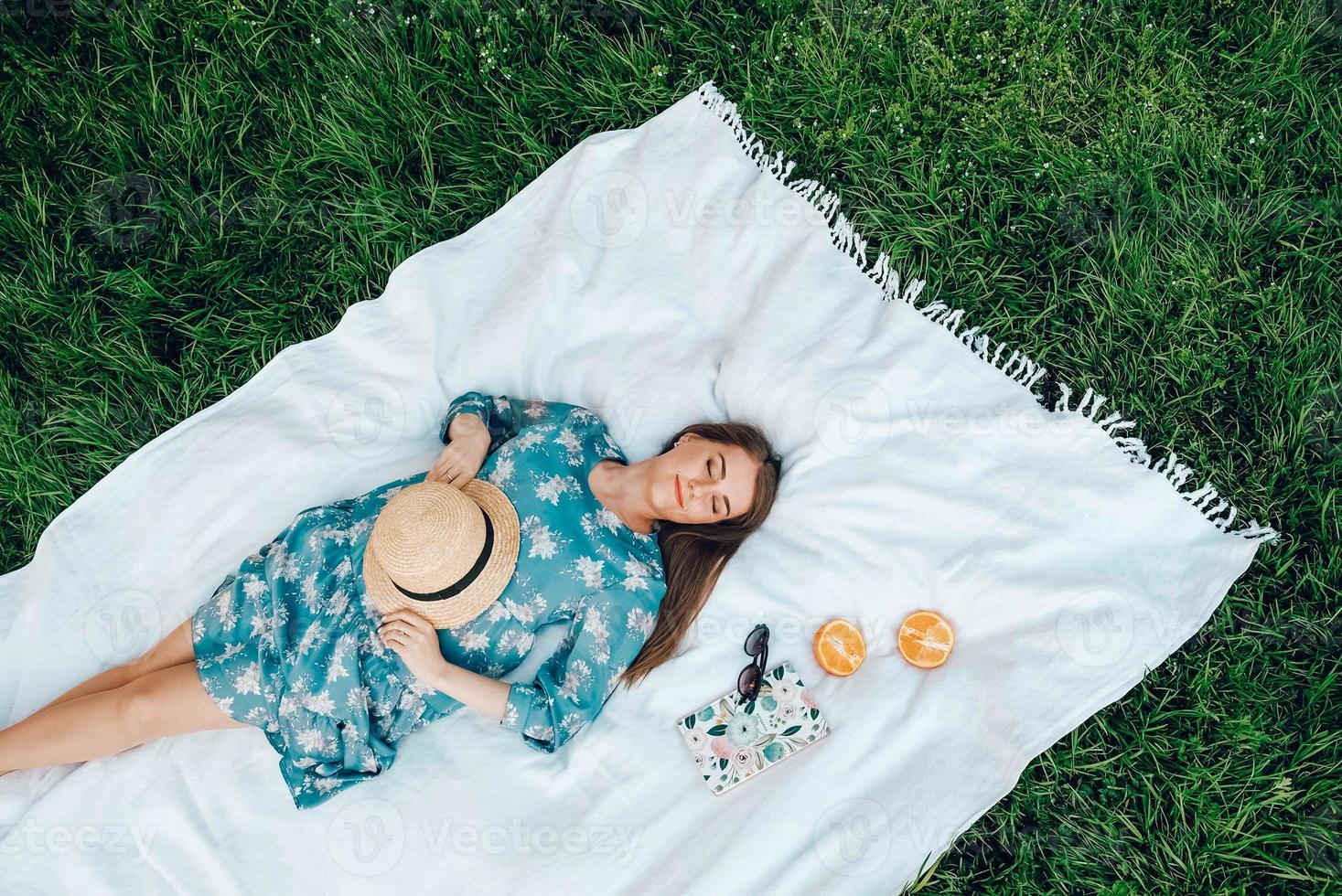 femme vêtue d'une robe colorée et d'un chapeau de paille se trouve sur une couverture blanche sur fond d'herbe verte, accessoires pour femmes, heure d'été photo