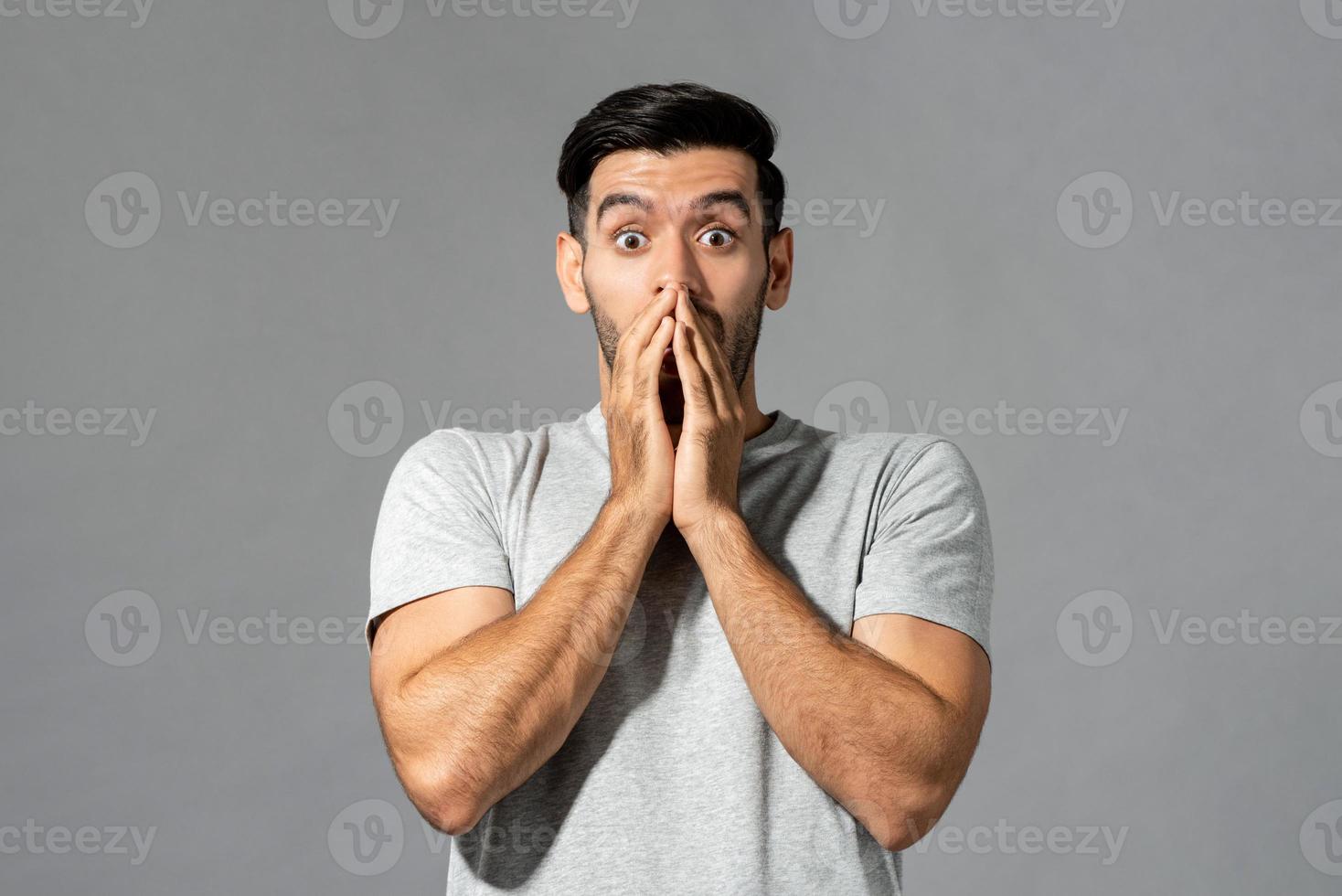 choqué jeune homme de race blanche avec les mains couvrant la bouche en arrière-plan studio gris clair isolé photo