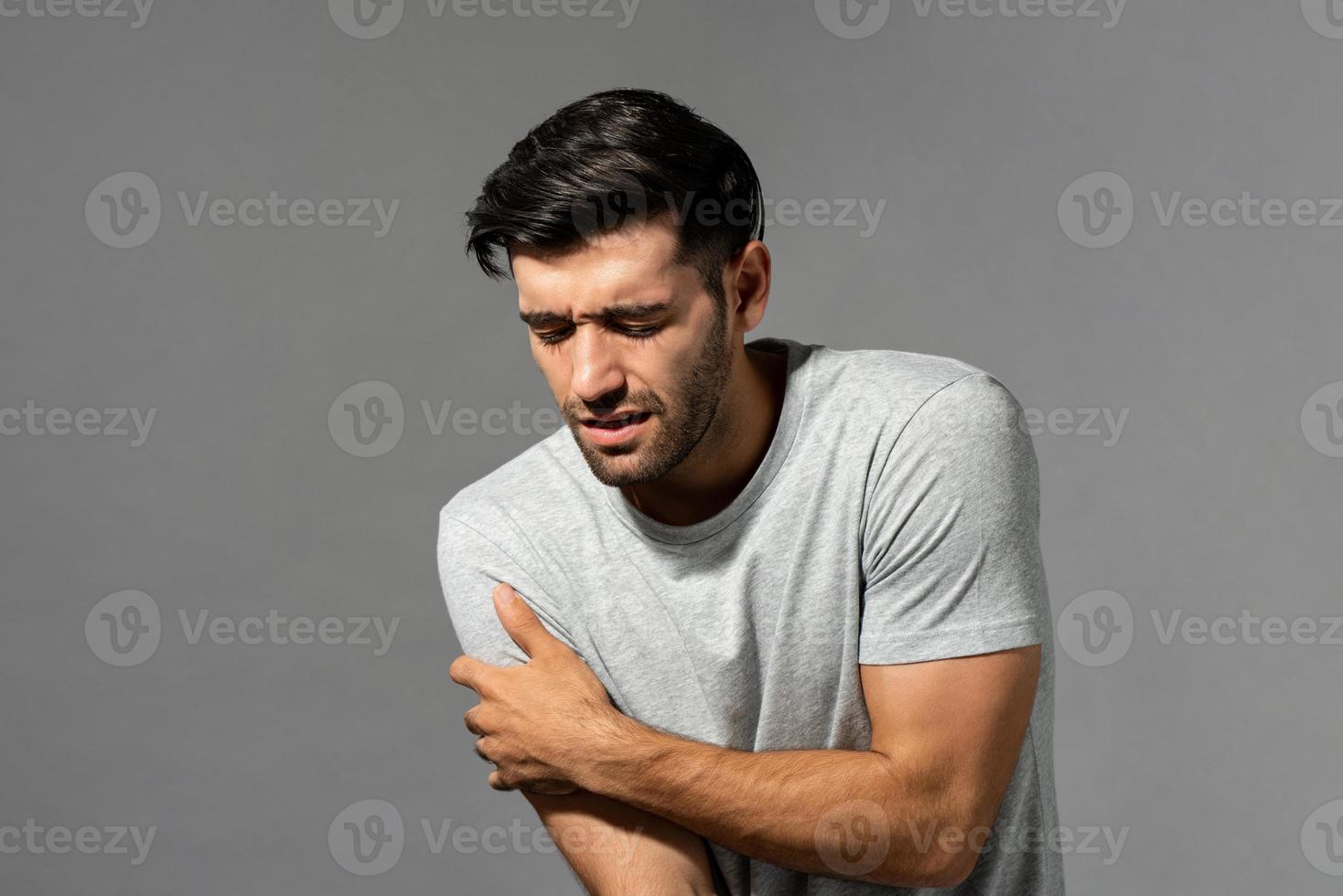 jeune homme de race blanche souffrant de douleurs à l'épaule, tourné en studio sur fond gris isolé photo