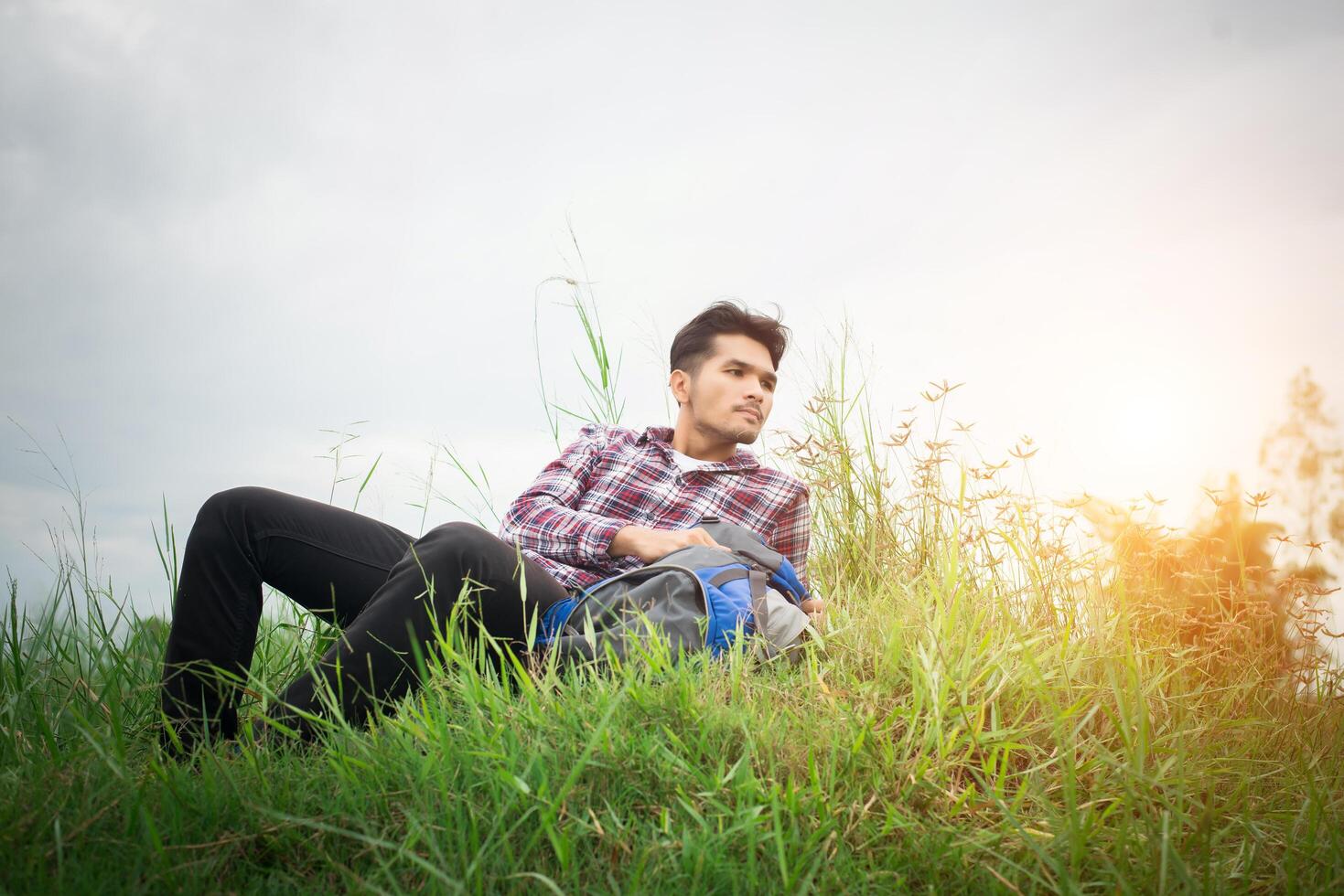 jeune homme hipster se reposer dans les prés après la randonnée, détourner le regard pour découvrir une autre aventure. photo