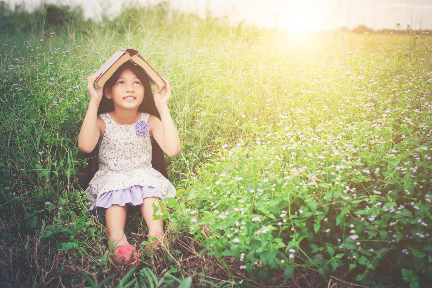 livre de couverture de petite fille asiatique mignonne sur sa tête à la nature. photo