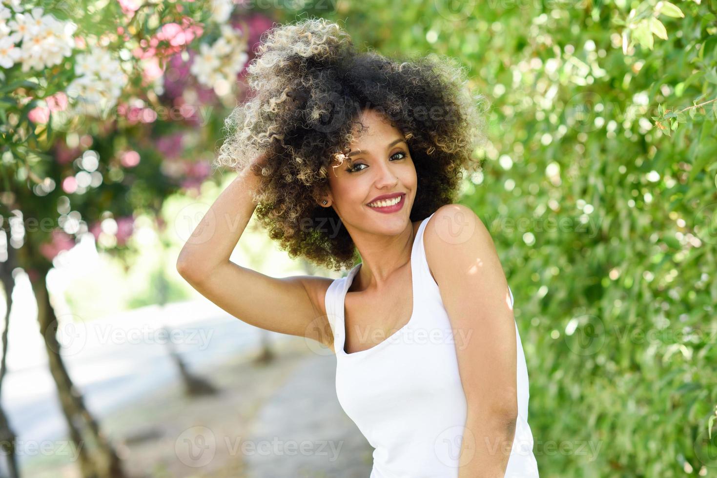 jeune femme noire avec une coiffure afro souriante dans un parc urbain photo