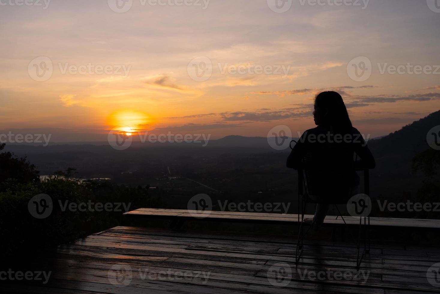 silhouette de femme assise sur la terrasse et regardant le coucher du soleil sur la montagne photo