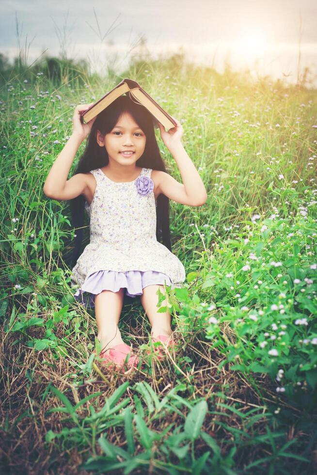 livre de couverture de petite fille asiatique mignonne sur sa tête à la nature. photo