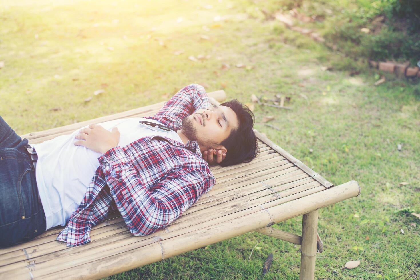 heureux jeune hipster allongé sur un banc dans le parc naturel. photo