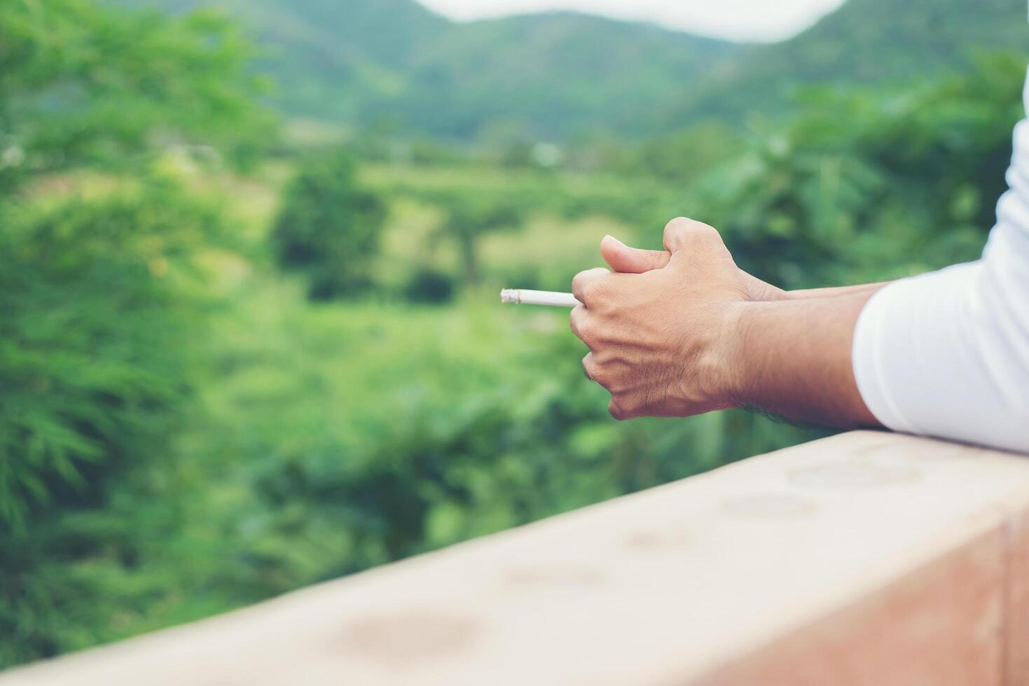 jeune homme hipster prenant du repos, fumant une cigarette avec la nature et la brise fraîche. photo