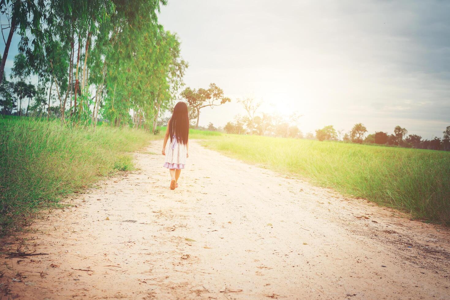 une petite fille aux cheveux longs en robe s'éloigne de vous sur une route rurale. photo