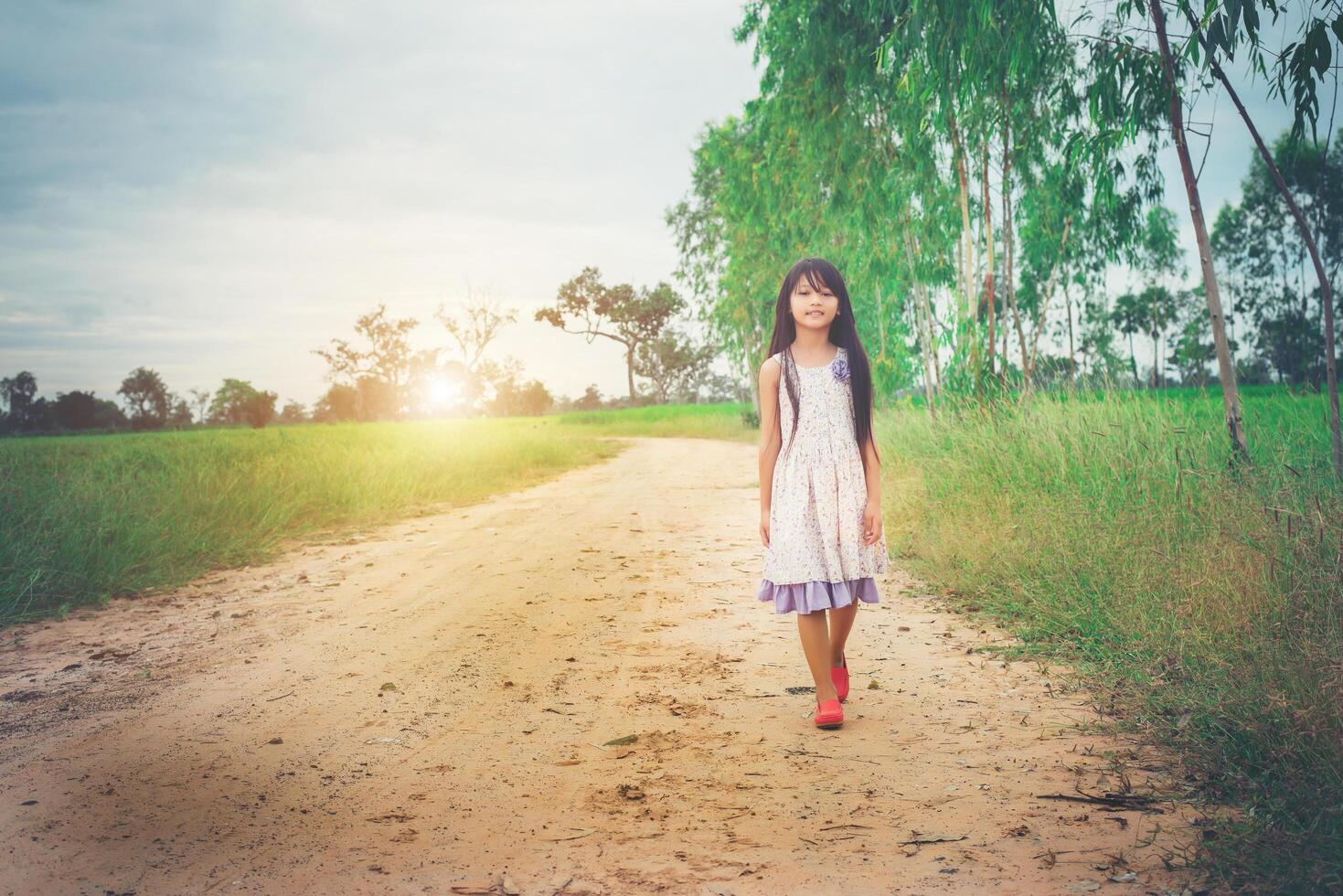 une petite fille aux cheveux longs en robe s'éloigne de vous sur une route rurale. photo