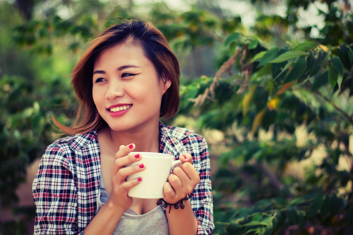 belle jeune femme heureuse tenant une tasse de café dans le parc. photo