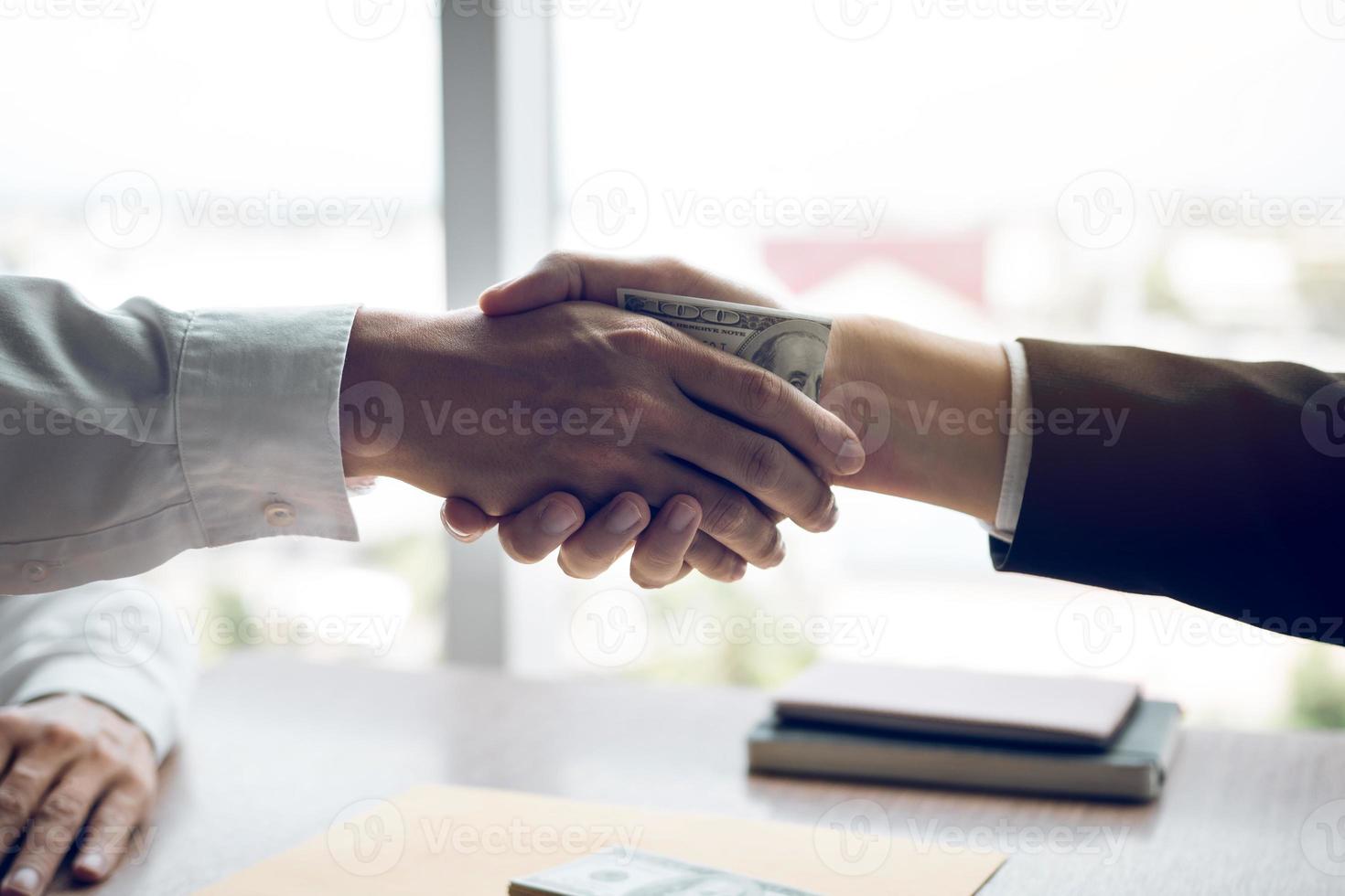 deux hommes d'affaires se serrant la main tandis qu'un homme place de l'argent sur un document dans une salle de bureau avec un concept de corruption. photo