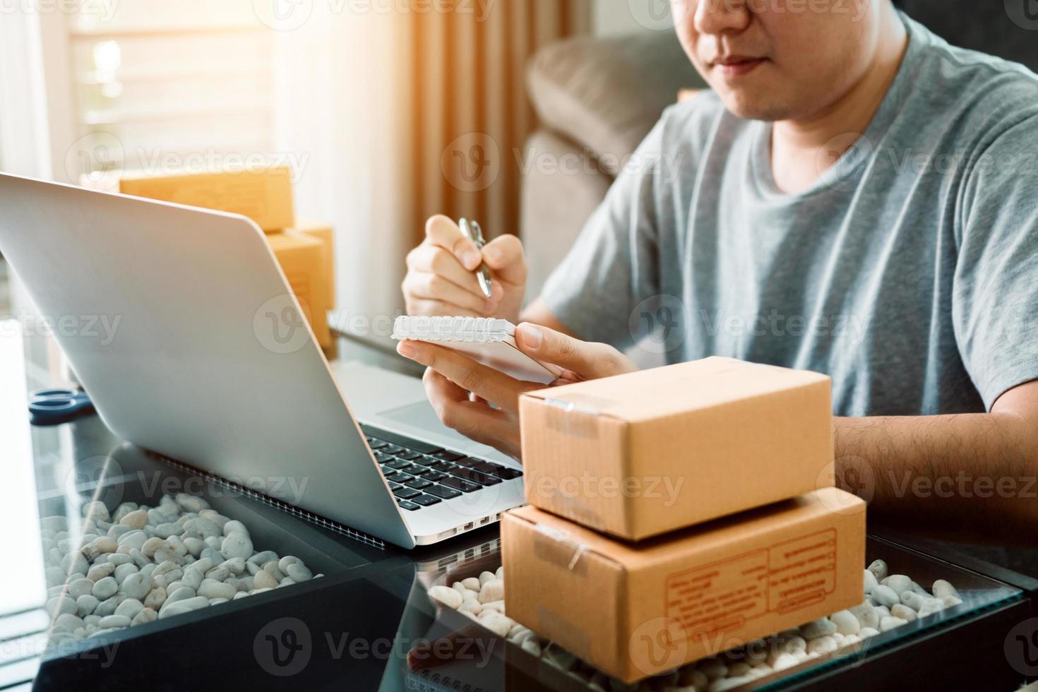 jeune homme asiatique regardant sur un ordinateur portable et écrivant une liste de commandes sur papier, concept de PME. photo