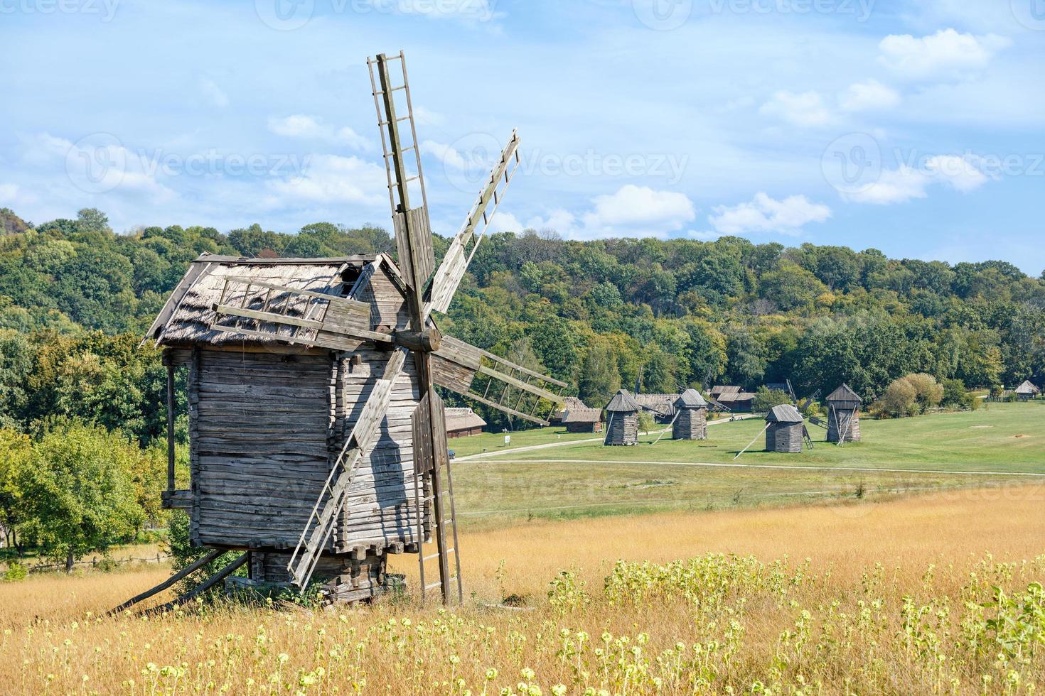 moulin à vent en bois antique sur fond de paysage d'été antique rural avec ciel bleu et forêt dense. photo