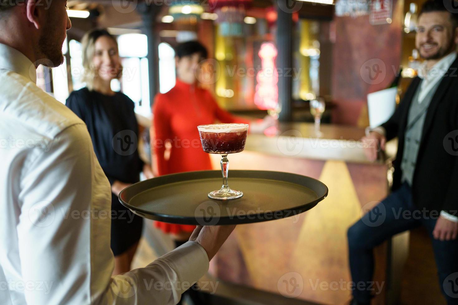 serveur servant un cocktail pour des clients élégants dans un joli bar photo
