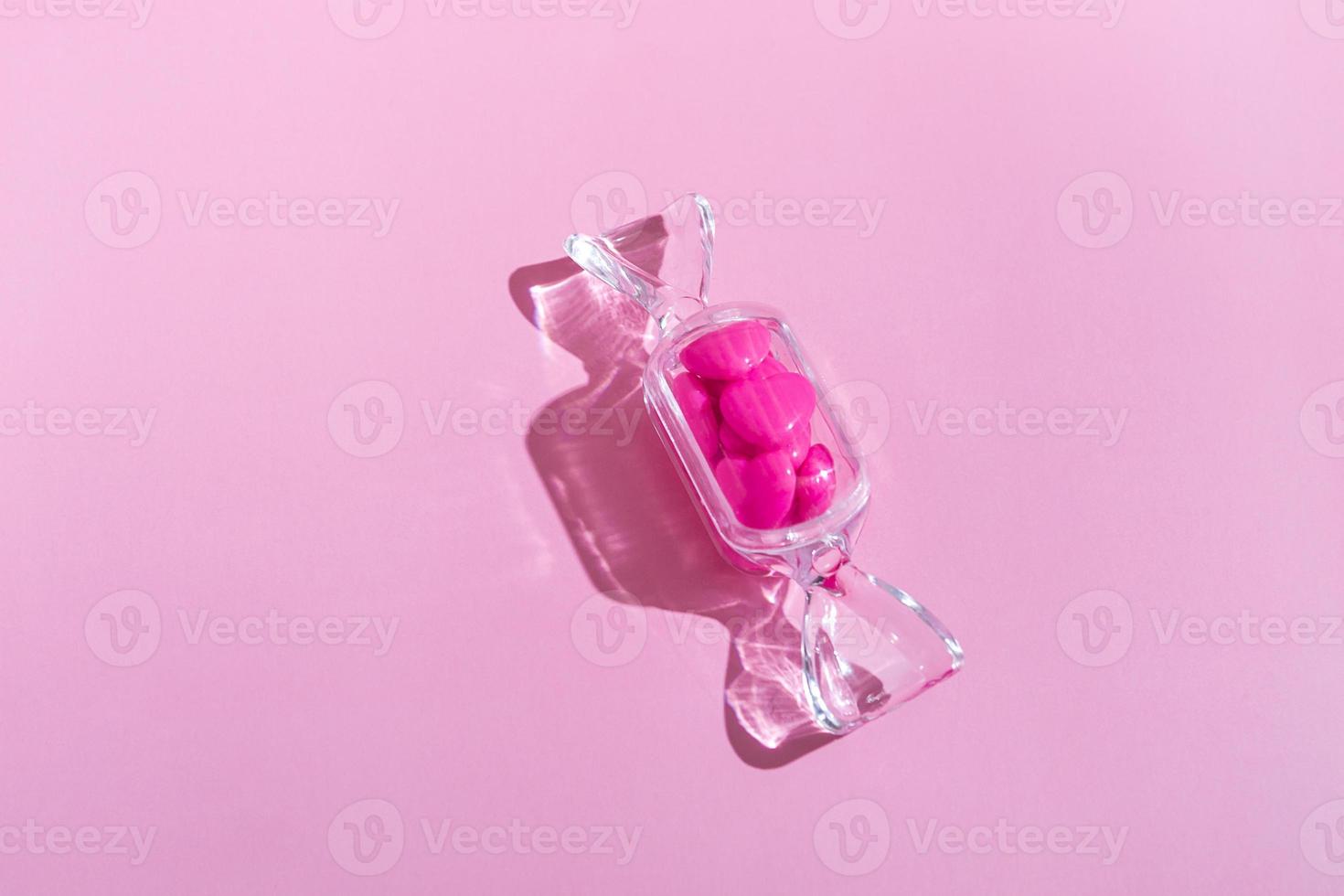 boîte transparente en forme de bonbon avec des sucettes au coeur doux avec une ombre dure sur fond rose avec espace de copie. le concept de la saint valentin, fête des mères. photo
