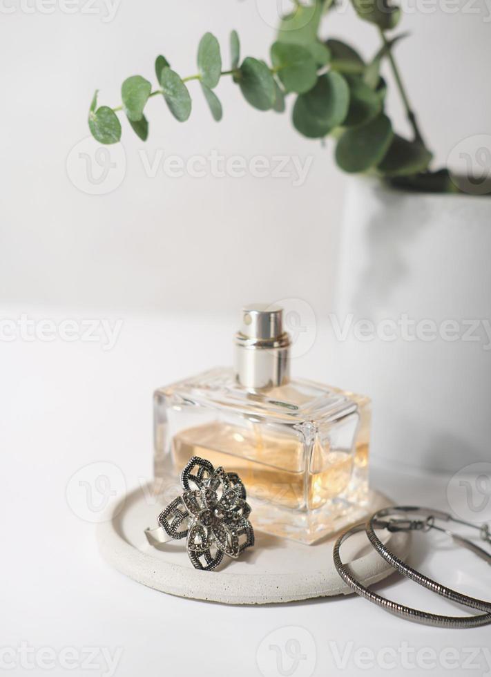 une bouteille de parfum et des bijoux sur une plaque de béton. accessoires de beauté pour femme. décor de table de lit femme. boucles d'oreilles et bague modernes photo