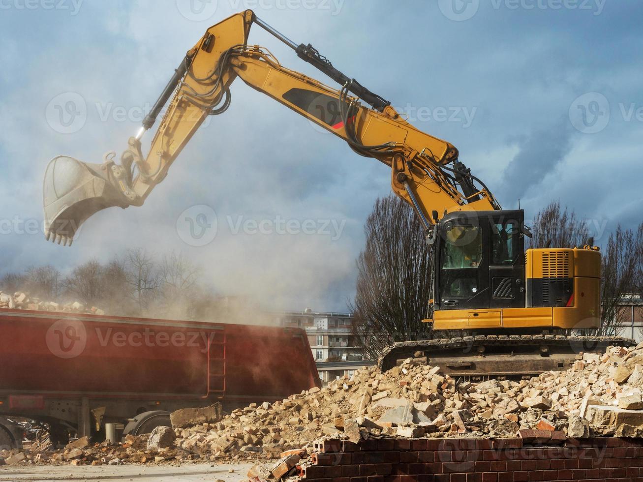 une excavatrice décompose un vieux bâtiment. poussière, briques et murs brisés. photo