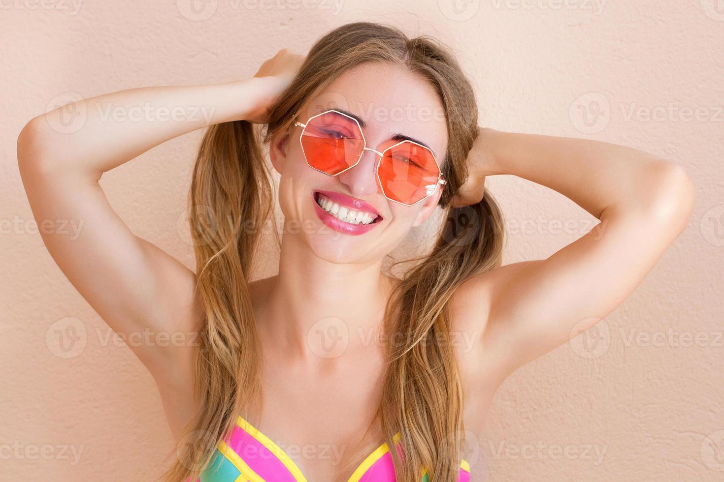 gros plan d'une fille heureuse en lunettes de soleil roses isolées. vacances d'été et week-end amusant. notion d'été. souriante jeune femme en maillot de bain fashion. mise au point sélective. style de tenue d'été de plage. photo