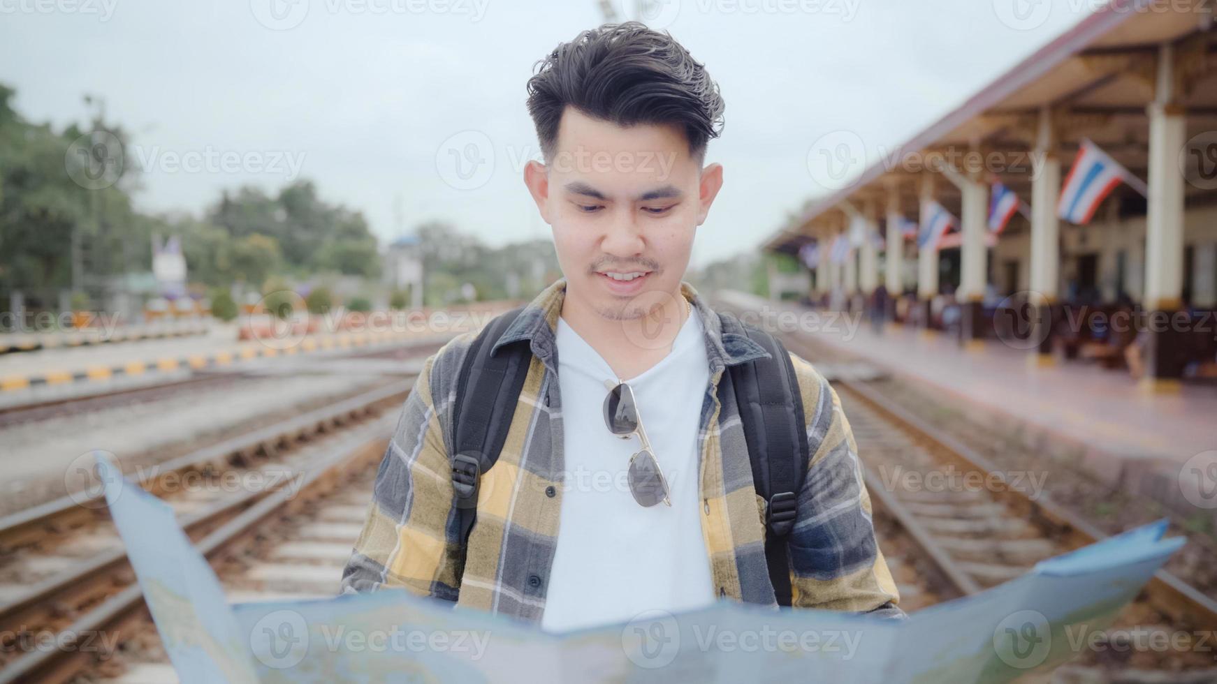 voyageur homme asiatique direction et regardant sur la carte de localisation tout en passant des vacances et en attendant le train à la gare, le jeune routard touristique masculin profite du voyage. concept de voyage d'hommes de style de vie. photo