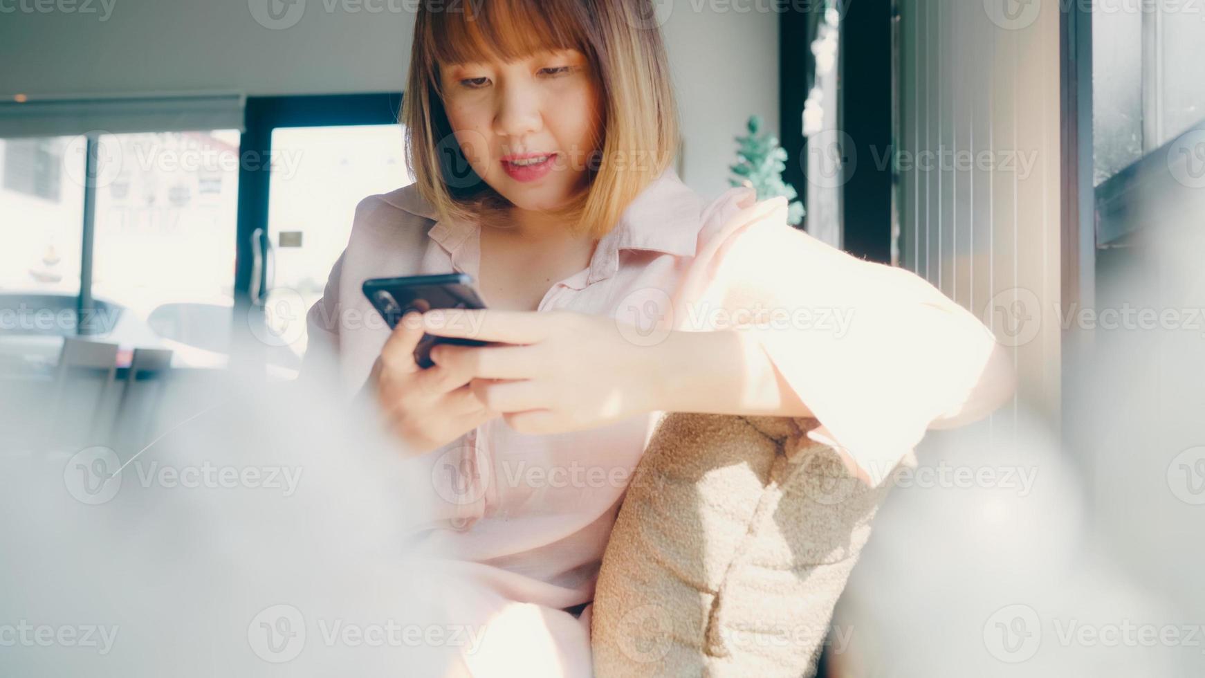 femme asiatique indépendante d'affaires utilisant un smartphone pour parler, lire et envoyer des SMS tout en étant assise sur une table dans un café. mode de vie intelligent belles femmes travaillant au concept de café. photo