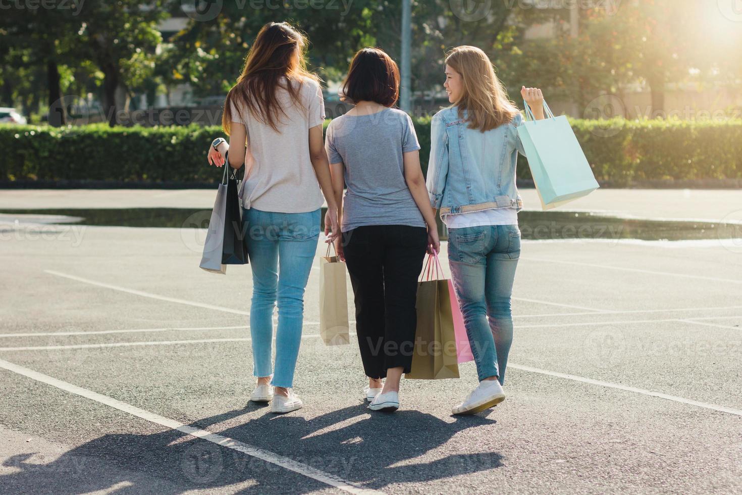 groupe de jeunes femmes asiatiques faisant du shopping dans un marché en plein air avec des sacs à provisions dans leurs mains. les jeunes femmes montrent ce qu'elles ont dans leur sac à provisions sous la chaleur du soleil. concept de shopping en plein air de groupe. photo