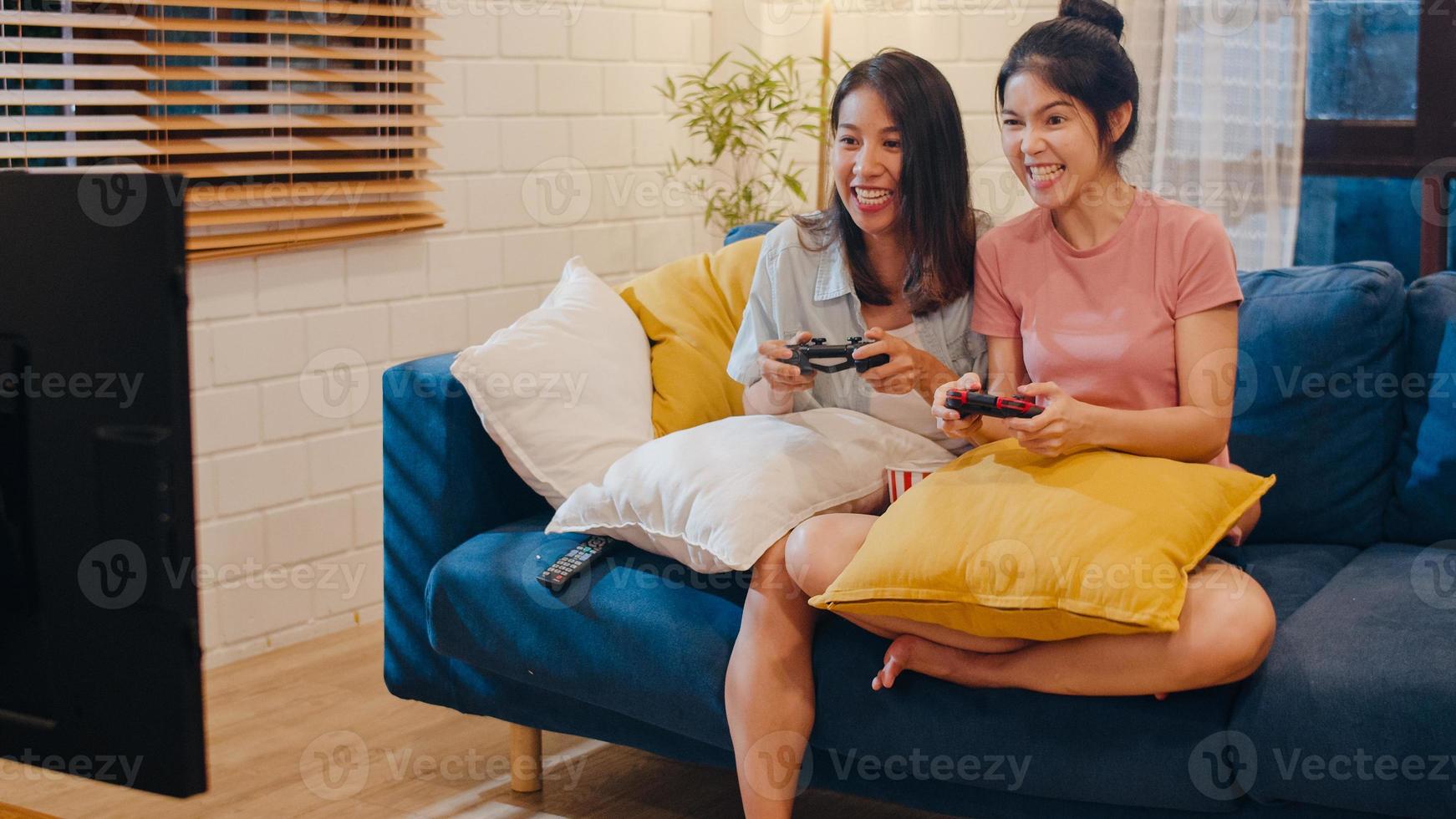 un couple de femmes lgbt lesbiennes joue à des jeux à la maison, une femme asiatique utilisant un joystick passe un moment amusant et heureux ensemble sur un canapé dans le salon la nuit. jeune amateur de football amateur, célèbre le concept de vacances. photo