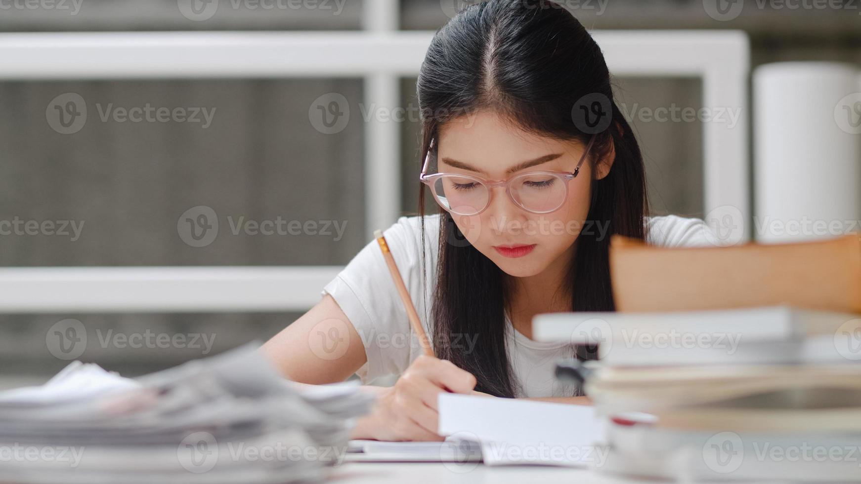 étudiantes asiatiques lisant des livres dans la bibliothèque de l'université. une jeune fille de premier cycle fait ses devoirs, lit des manuels, étudie dur pour acquérir des connaissances et de l'éducation sur un pupitre de conférence sur le campus universitaire. photo