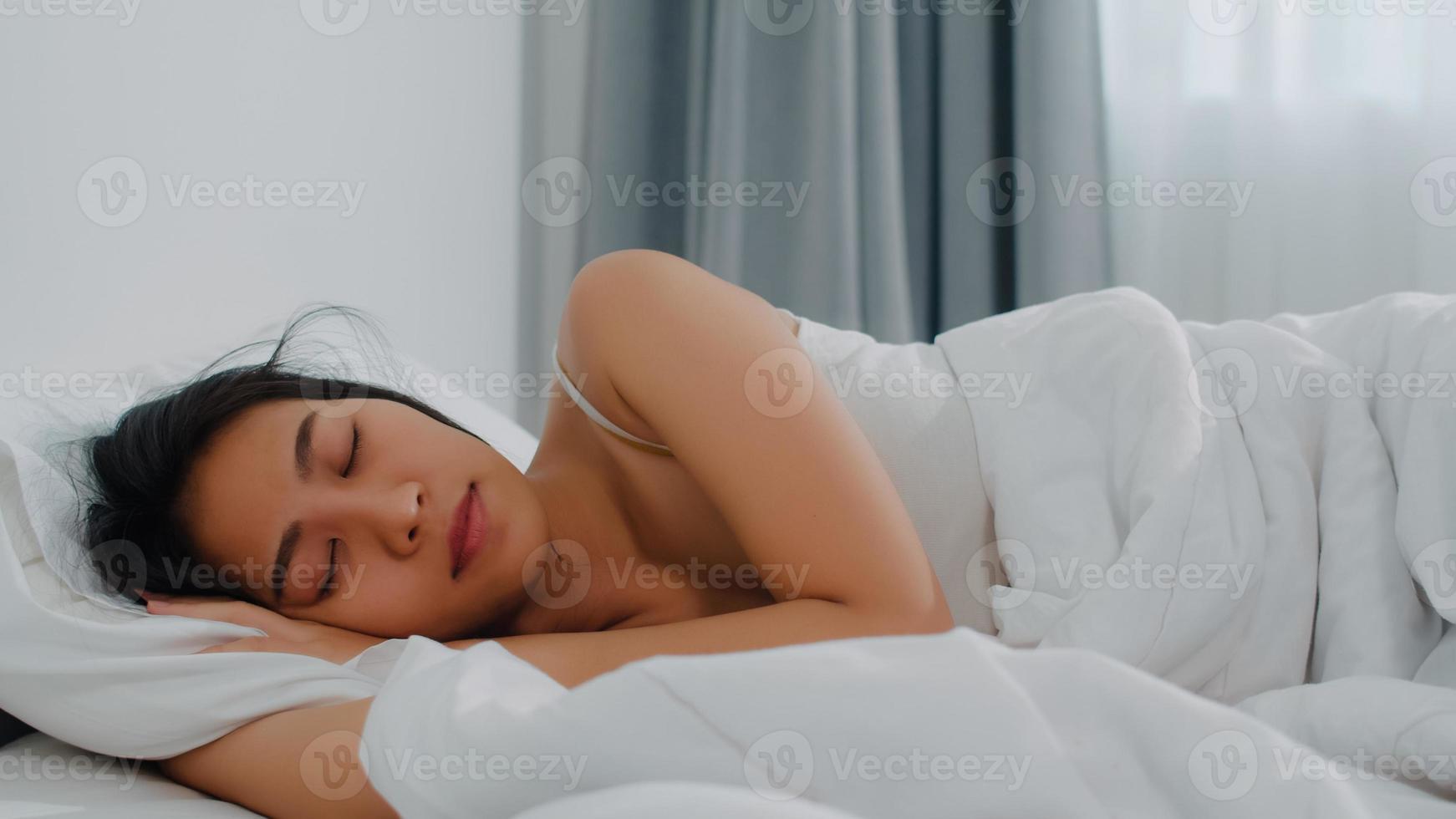 dame indienne asiatique dort dans la chambre à la maison. jeune fille asiatique se sentant heureuse se détendre se reposer allongée sur le lit, se sentir à l'aise et calme dans la chambre à la maison le matin. photo