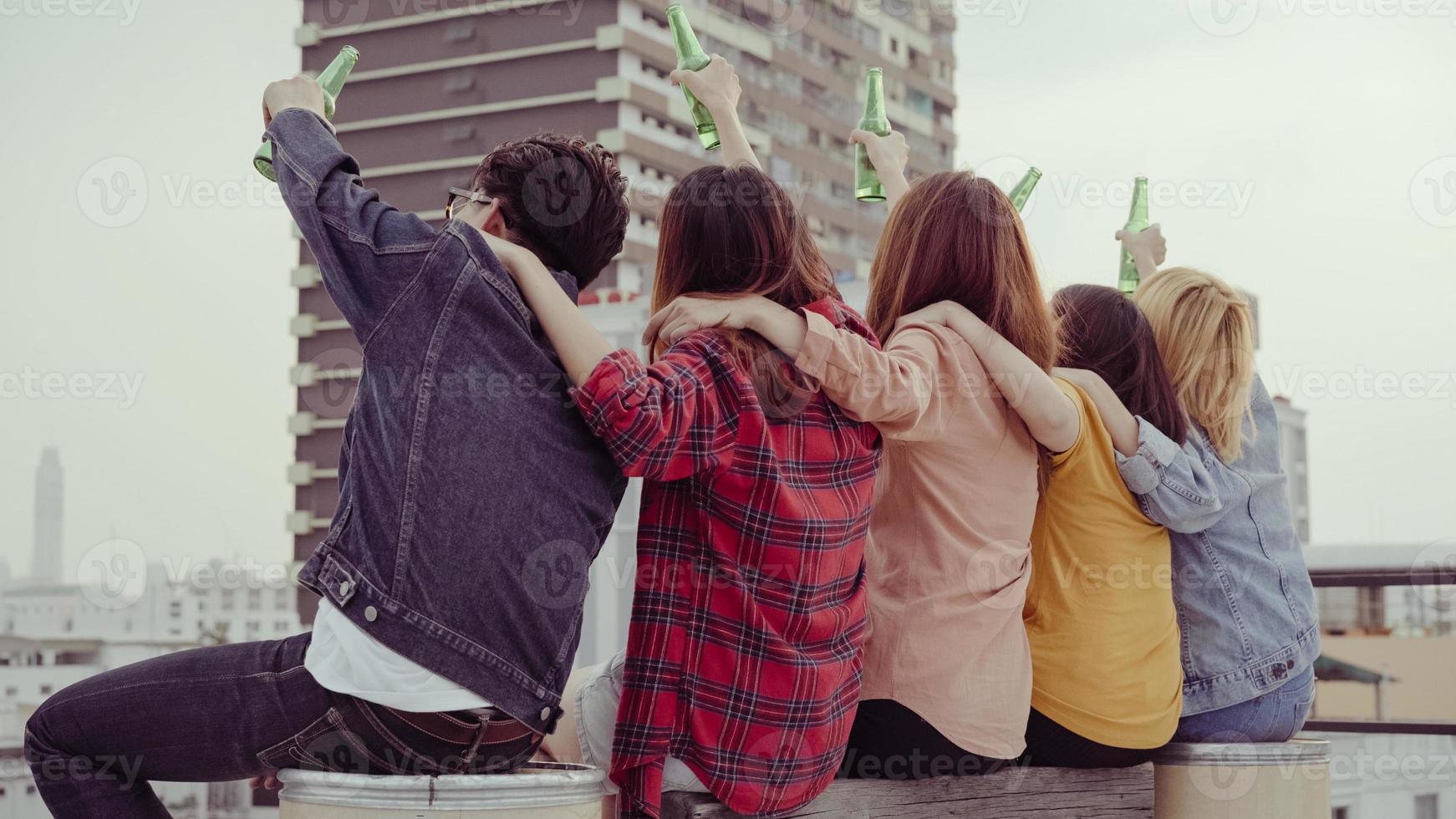 groupe de jeunes femmes asiatiques et hommes dansant et levant les bras en l'air sur la musique jouée par dj au coucher du soleil fête urbaine sur le toit. jeunes filles asiatiques et amis garçons traîner avec des boissons photo