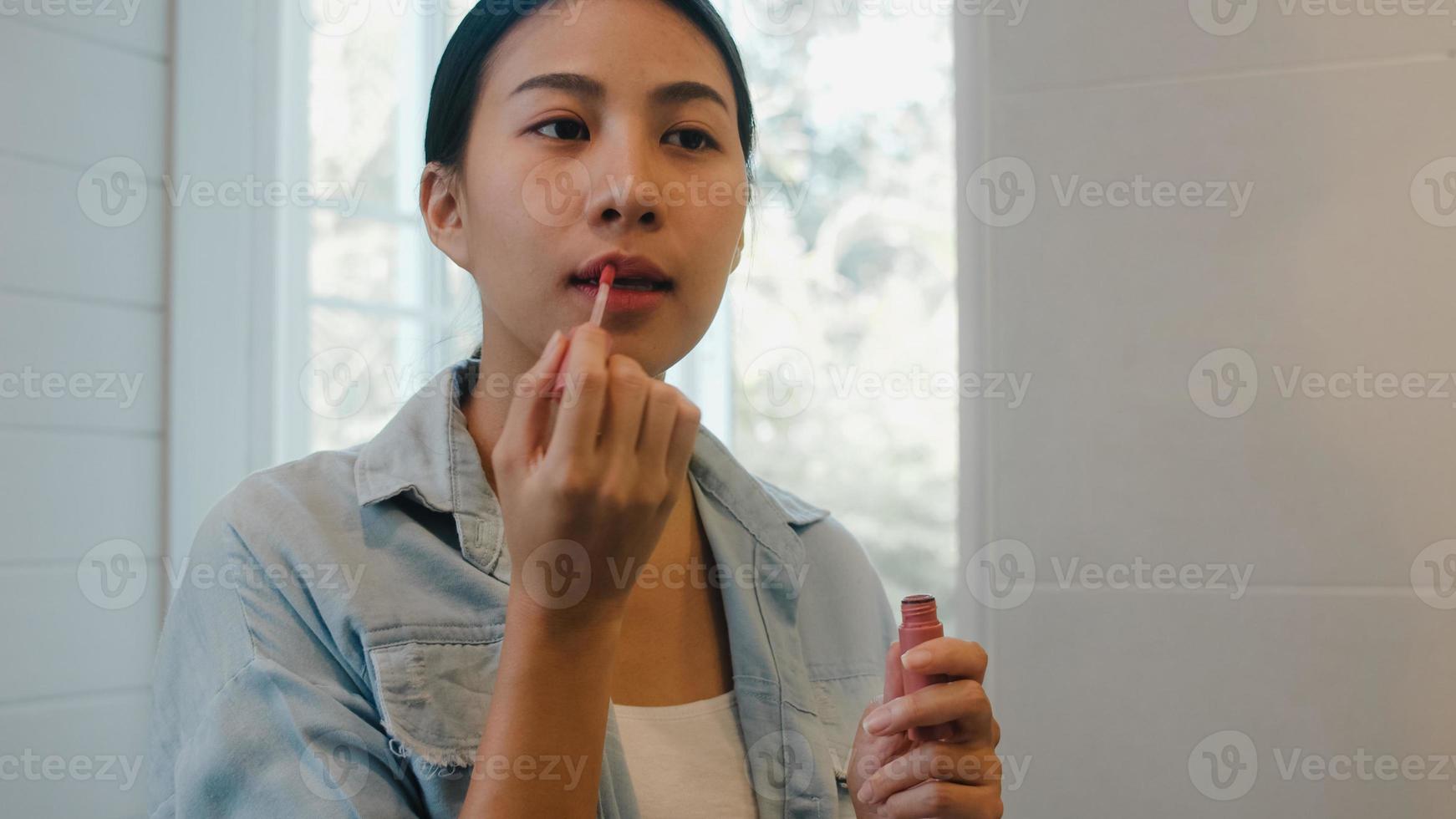 belle femme asiatique utilisant du rouge à lèvres maquillage devant le miroir, heureuse femme chinoise utilisant des cosmétiques de beauté pour s'améliorer prête à travailler dans la salle de bain à la maison. les femmes de style de vie se détendent à la maison concept photo