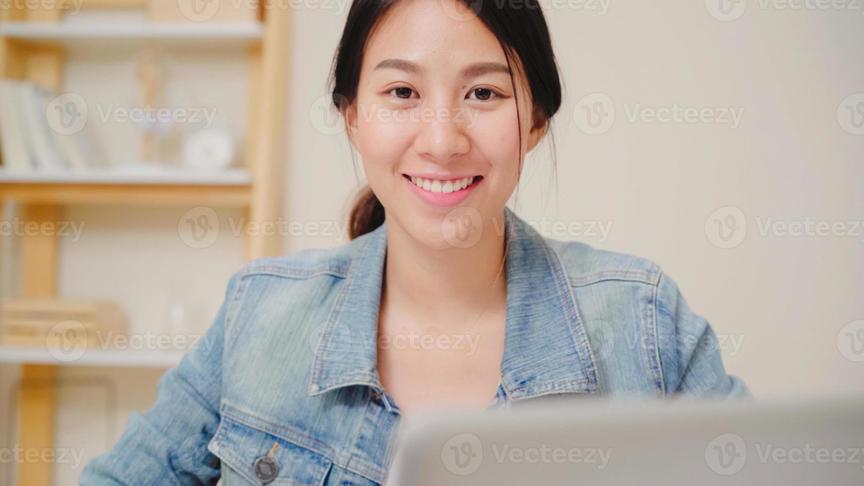 femme d'affaires d'asie se sentant heureuse en souriant et en regardant la caméra tout en se détendant au bureau à domicile. jeune femme asiatique travaillant à l'aide d'un ordinateur portable sur le bureau dans le salon à la maison. photo