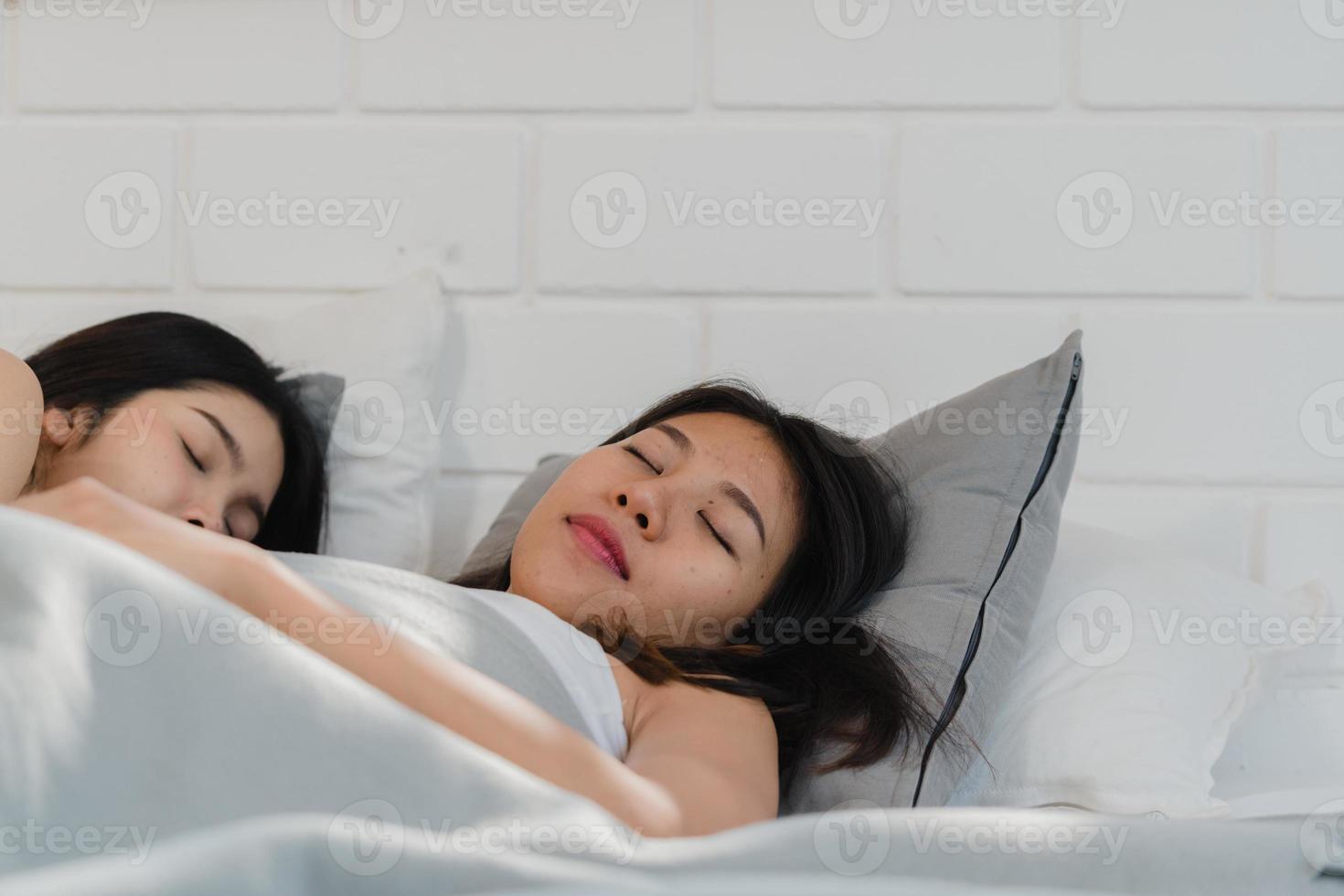 un couple de lesbiennes asiatiques dort ensemble à la maison. les jeunes femmes asiatiques lgbtq heureuses se détendent allongées sur le lit dans la chambre à la maison le matin. photo