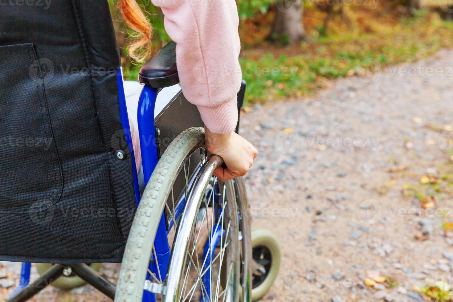 femme handicapée à la main dans la roue de fauteuil roulant sur la route dans le parc de l'hôpital en attente de services aux patients. fille paralysée méconnaissable dans une chaise invalide pour personnes handicapées à l'extérieur. notion de réhabilitation. photo