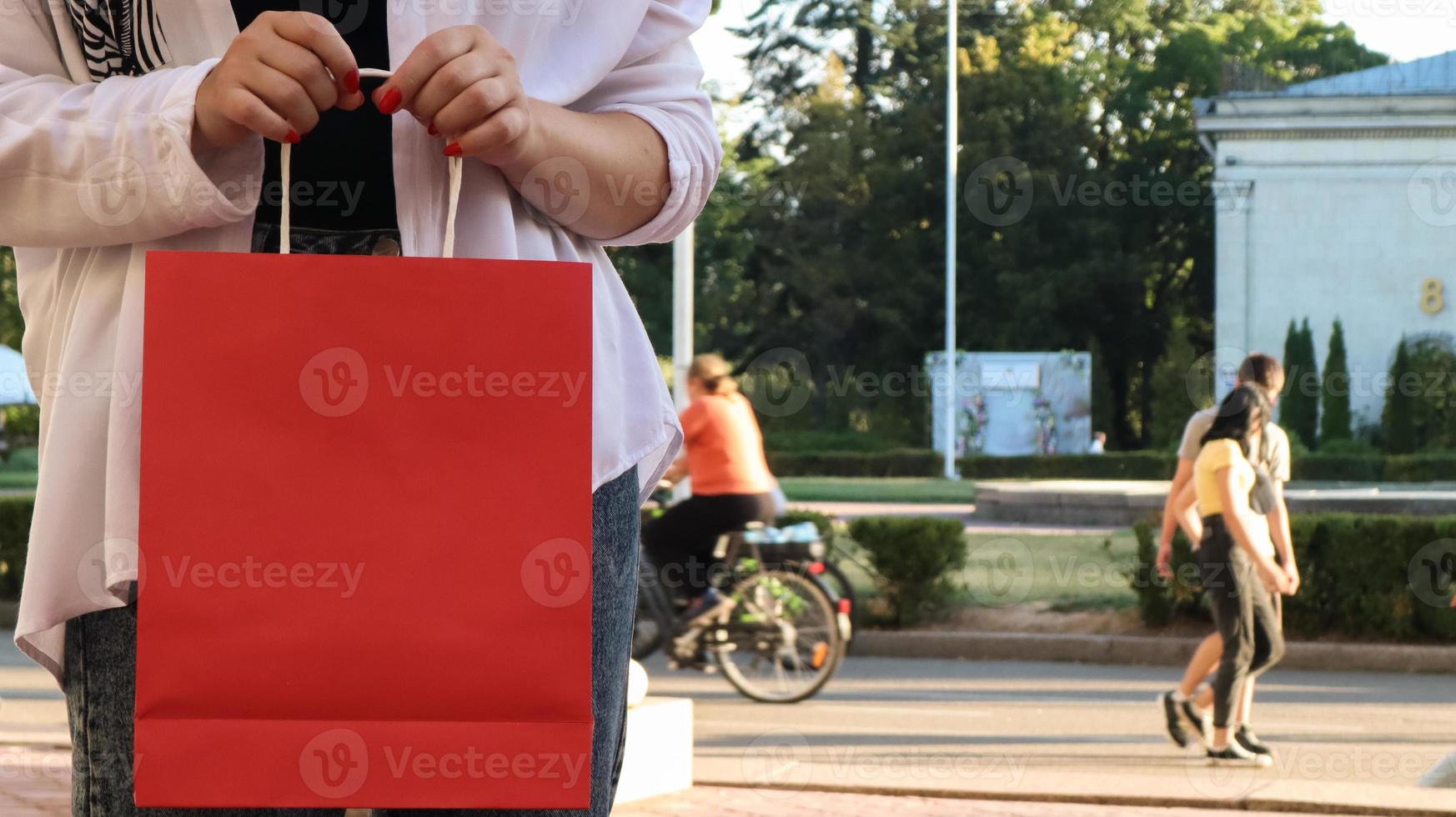 gros plan d'une femme accro du shopping avec un sac à provisions en papier rouge dans les mains. recadrer la photo. consumérisme, shopping, concept de style de vie. copiez l'espace pour votre logo. vendredi noir photo