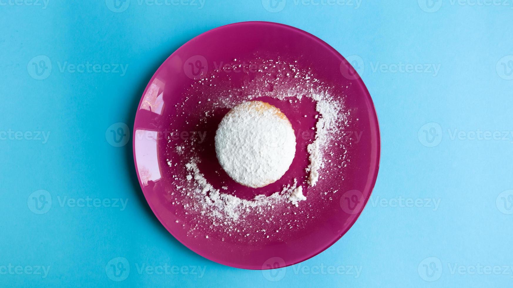saupoudrer un fromage cottage de sucre en poudre sur une assiette rose, sur fond bleu, vue de dessus. dessert, un petit gâteau. notion de nourriture. biscuits blancs cuits au four avec une texture aérée. copie espace photo