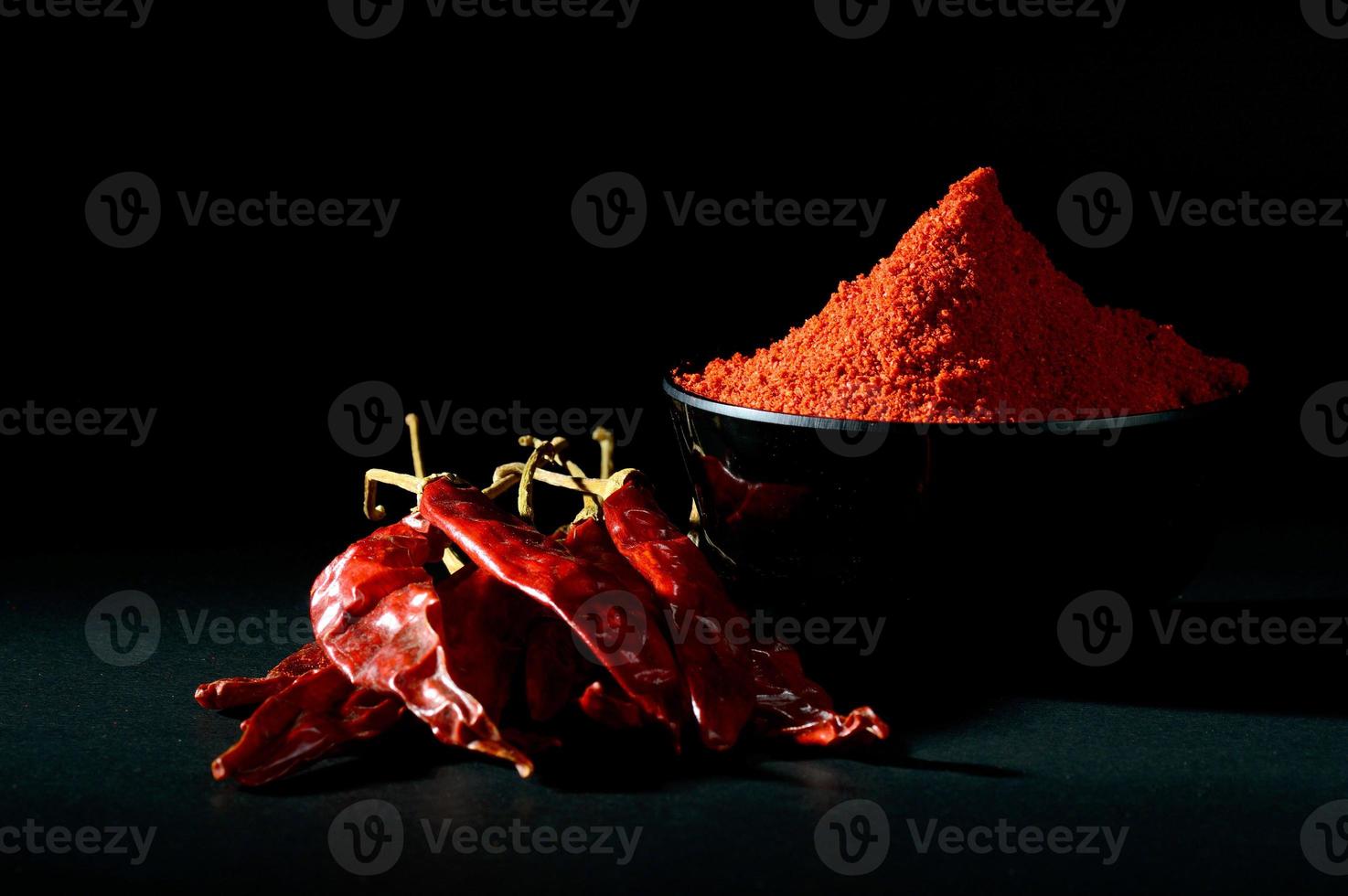 poudre froide dans un bol noir avec des piments rouges frais et séchés sur fond noir photo