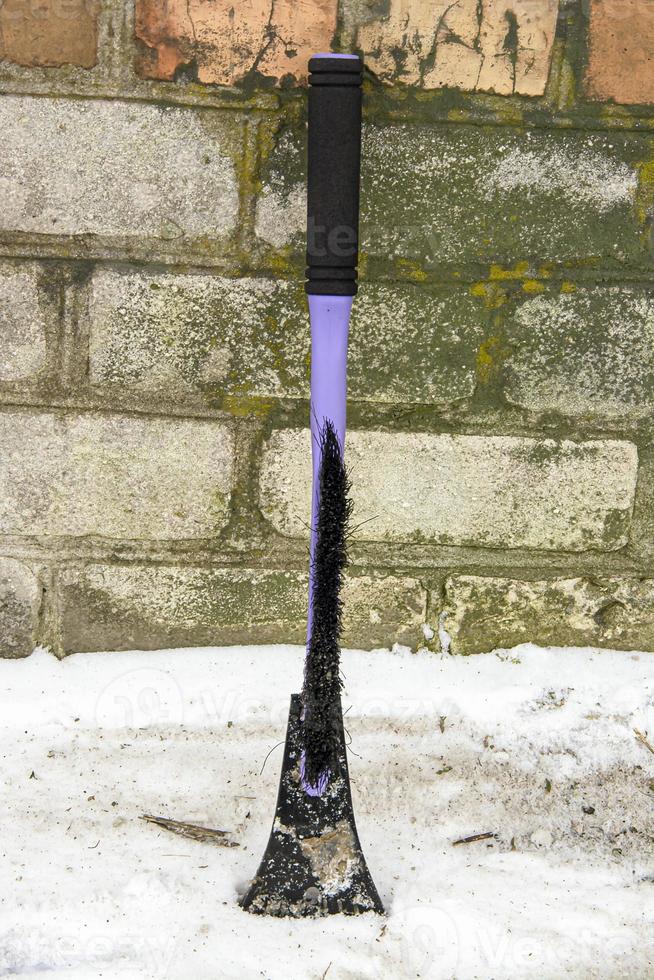 brosse à gratter pour nettoyer la saleté et la neige sur le fond du mur de briques du garage. photo