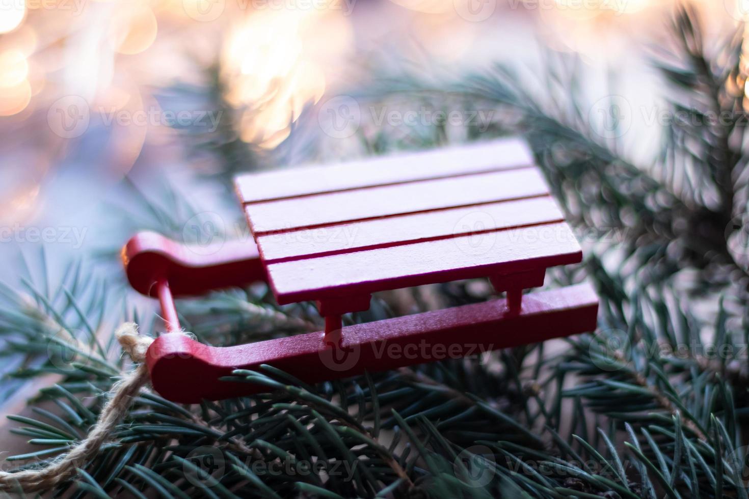 jouet d'arbre de noël petit traîneau en bois rouge sur le fond d'un arbre de noël et de guirlandes photo