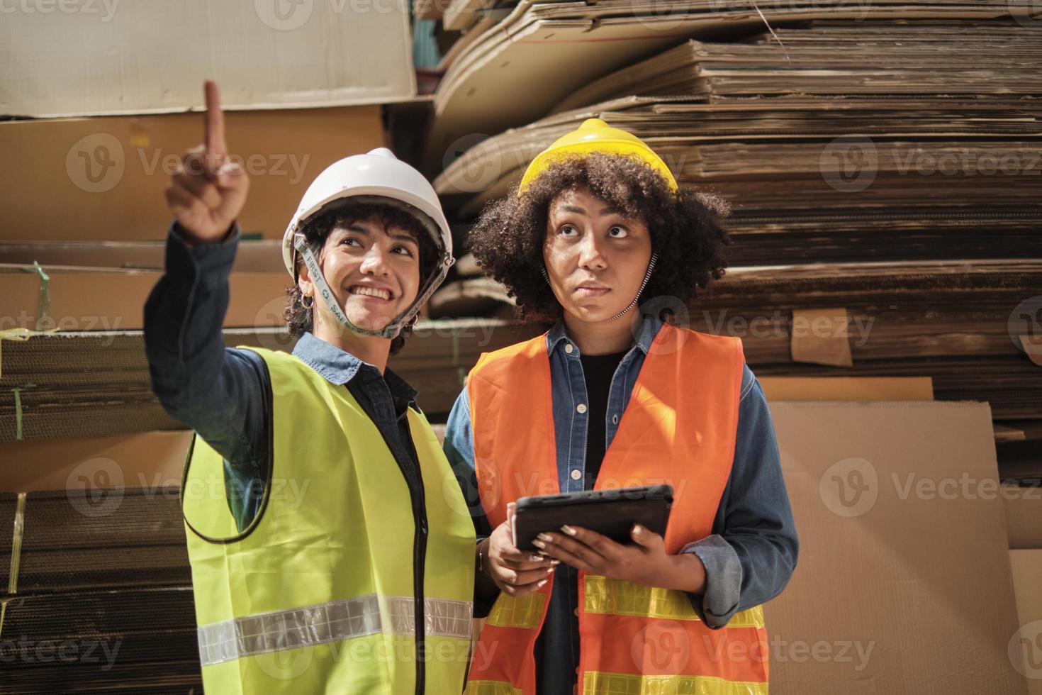 deux travailleuses et collègues en uniformes de sécurité et vérification des stocks de casques, contrôlent la production dans le stockage de l'usine d'entrepôt avec beaucoup de pile de papier, un ami travaille dans une entreprise de fabrication de recyclage. photo
