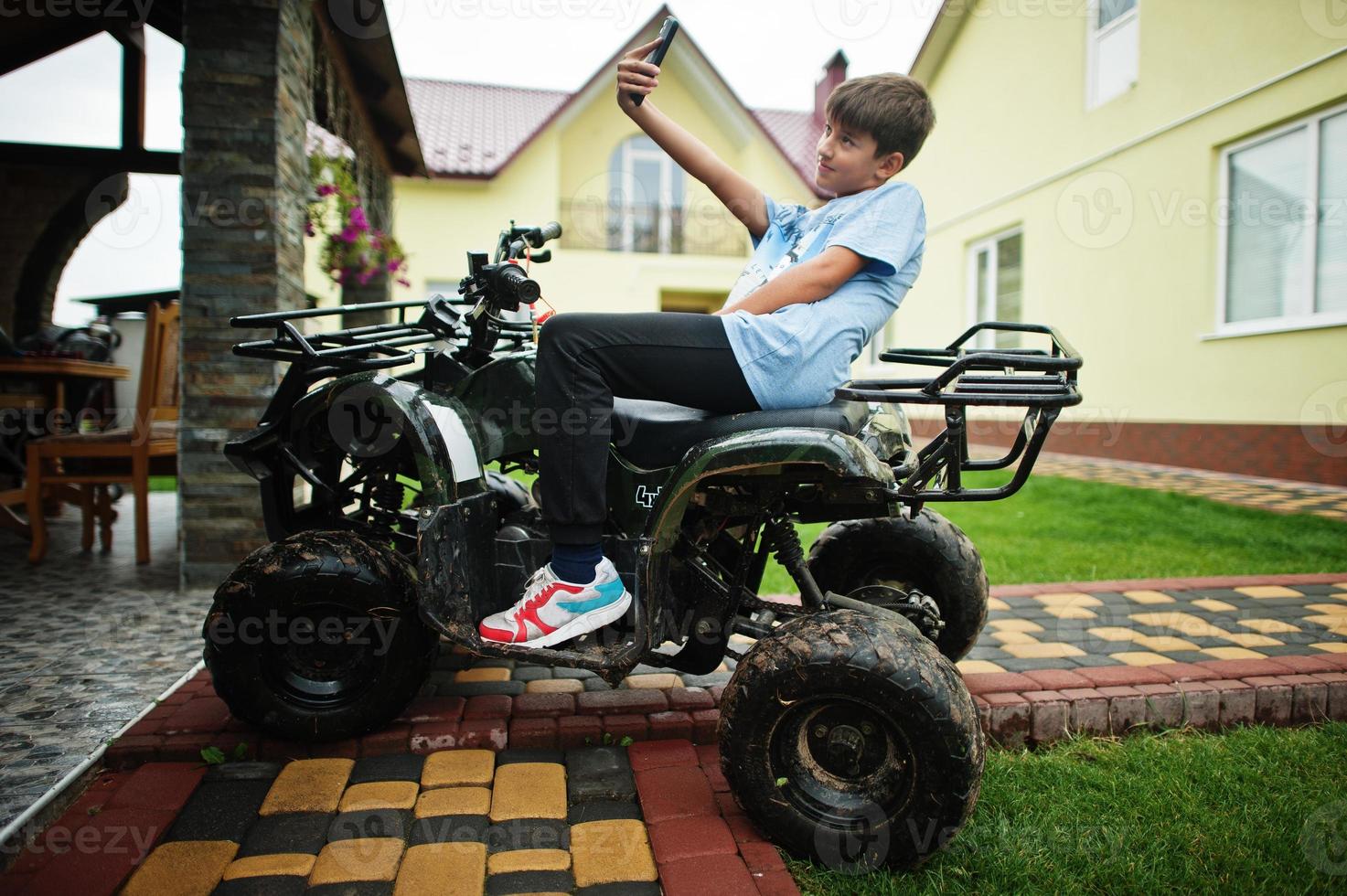 garçon en quad quad à quatre roues avec téléphone portable. photo