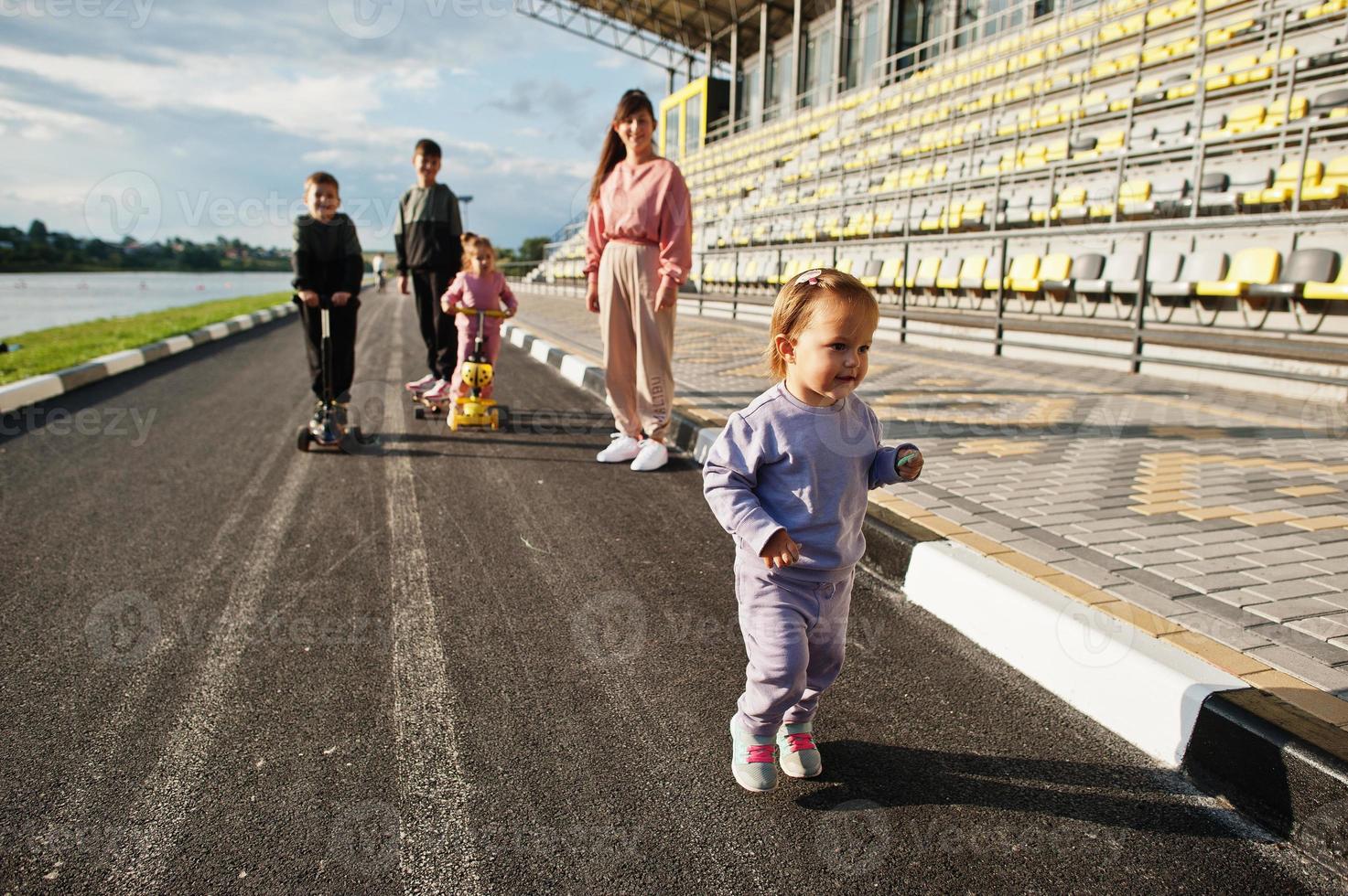 jeune mère élégante avec quatre enfants en plein air. la famille sportive passe du temps libre à l'extérieur avec des scooters et des patins. photo