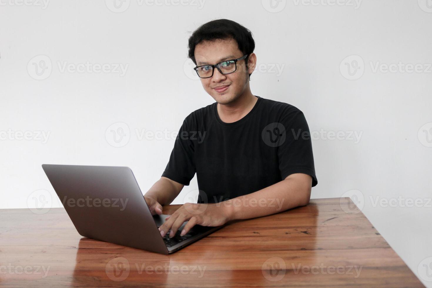 le jeune homme asiatique est un travail sérieux ou pense devant l'ordinateur portable. l'homme indonésien porte une chemise noire isolée sur fond gris. photo