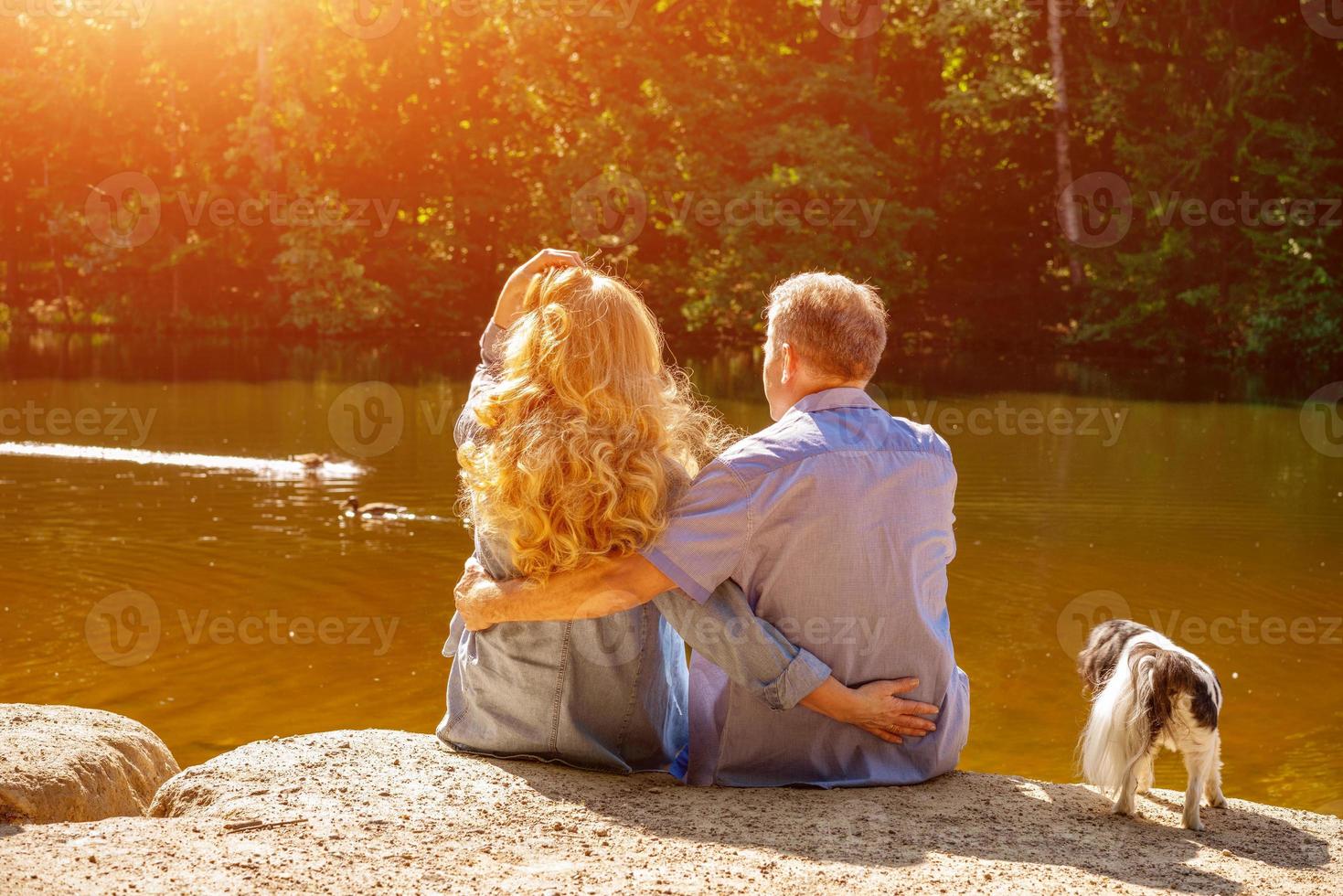 heureux couple mature assis sur le lac au soleil avec leurs chiens. concept de vacances en famille dans la nature photo