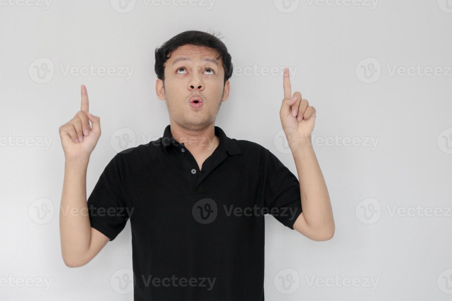 visage heureux et souriant avec le sourire d'un jeune homme asiatique en chemise noire avec la main pointée au-dessus de l'espace vide. photo