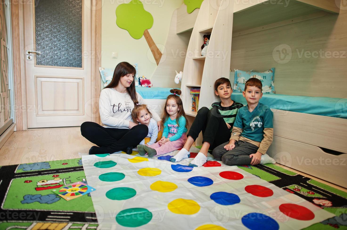 famille heureuse s'amusant ensemble, quatre enfants et leur mère jouant au jeu de twister à la maison. photo