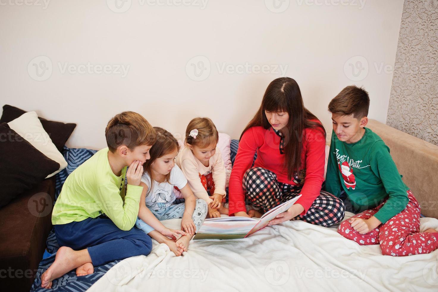 une grande famille heureuse s'amuse ensemble dans la chambre. grand concept de matinée familiale. mère de quatre enfants porte un pyjama lit un livre au lit à la maison. photo