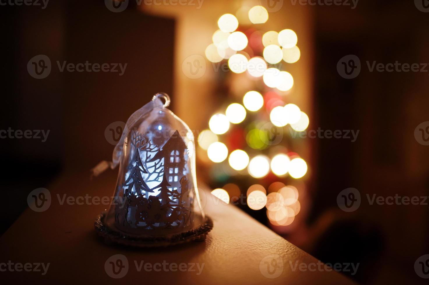 cloche lumineuse contre le sapin de noël avec des guirlandes brillantes le soir à la maison. photo